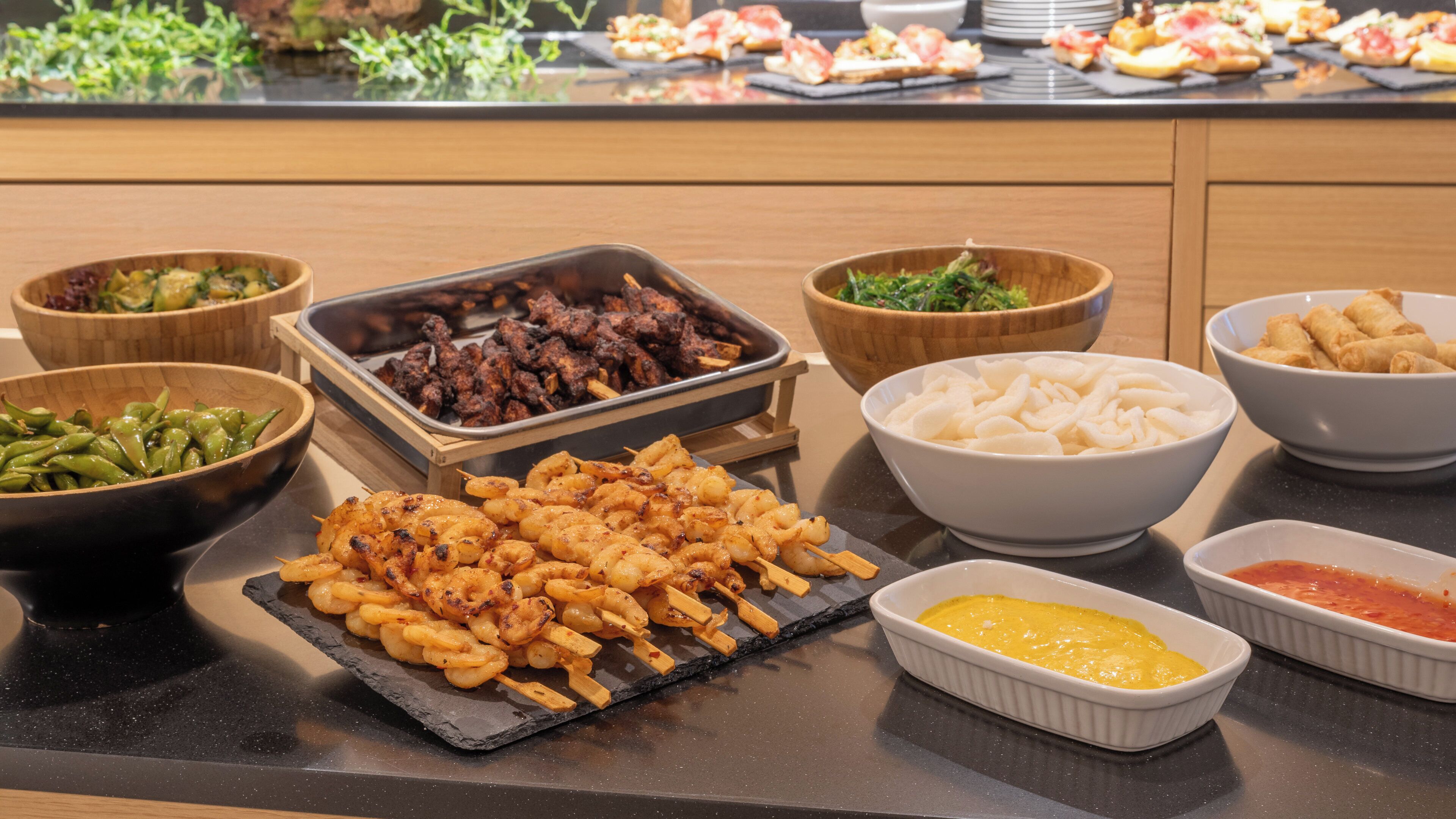 Un buffet proposant une variété de plats, notamment des brochettes de crevettes, de la viande grillée et des légumes.