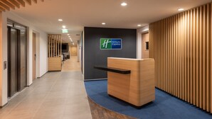 A modern hotel reception area with a wooden reception desk, a Holiday Inn Express sign, and a ceiling with a perforated pattern. - Holiday Inn Express Hamburg South A7 AS42 by IHG (Egestorf)