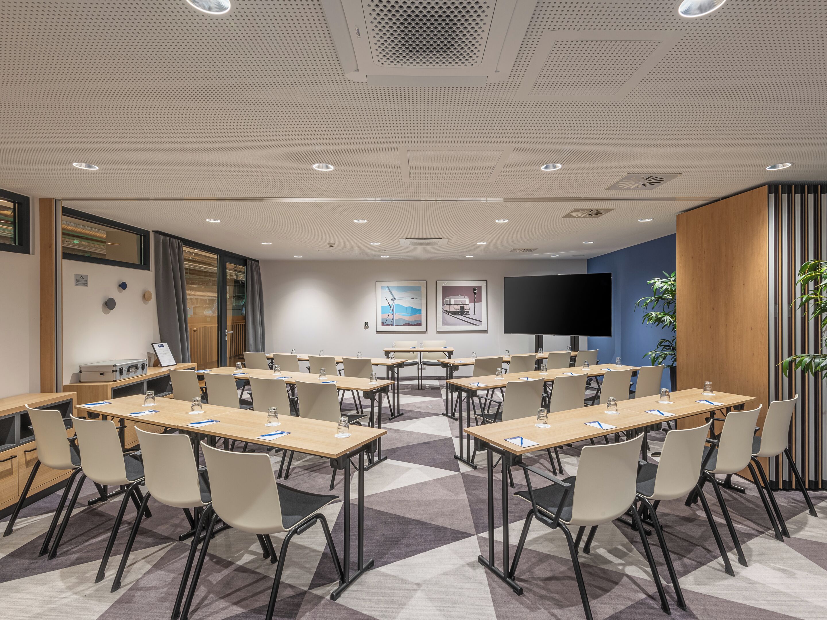 A conference room with multiple tables, chairs, a large flat-screen TV, and framed artwork on the walls.