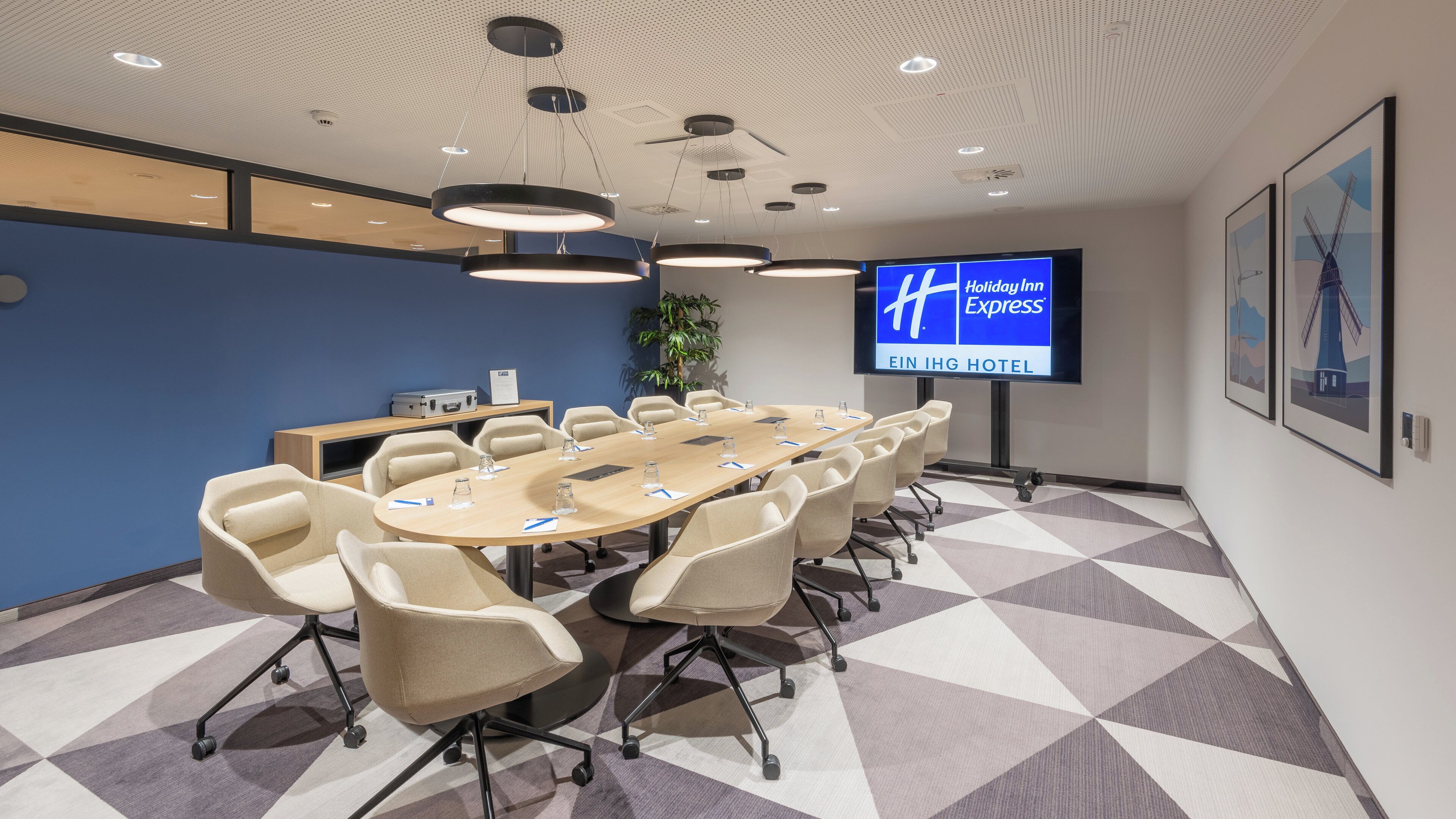 A conference room with a long table, chairs, a television screen, and a plant.