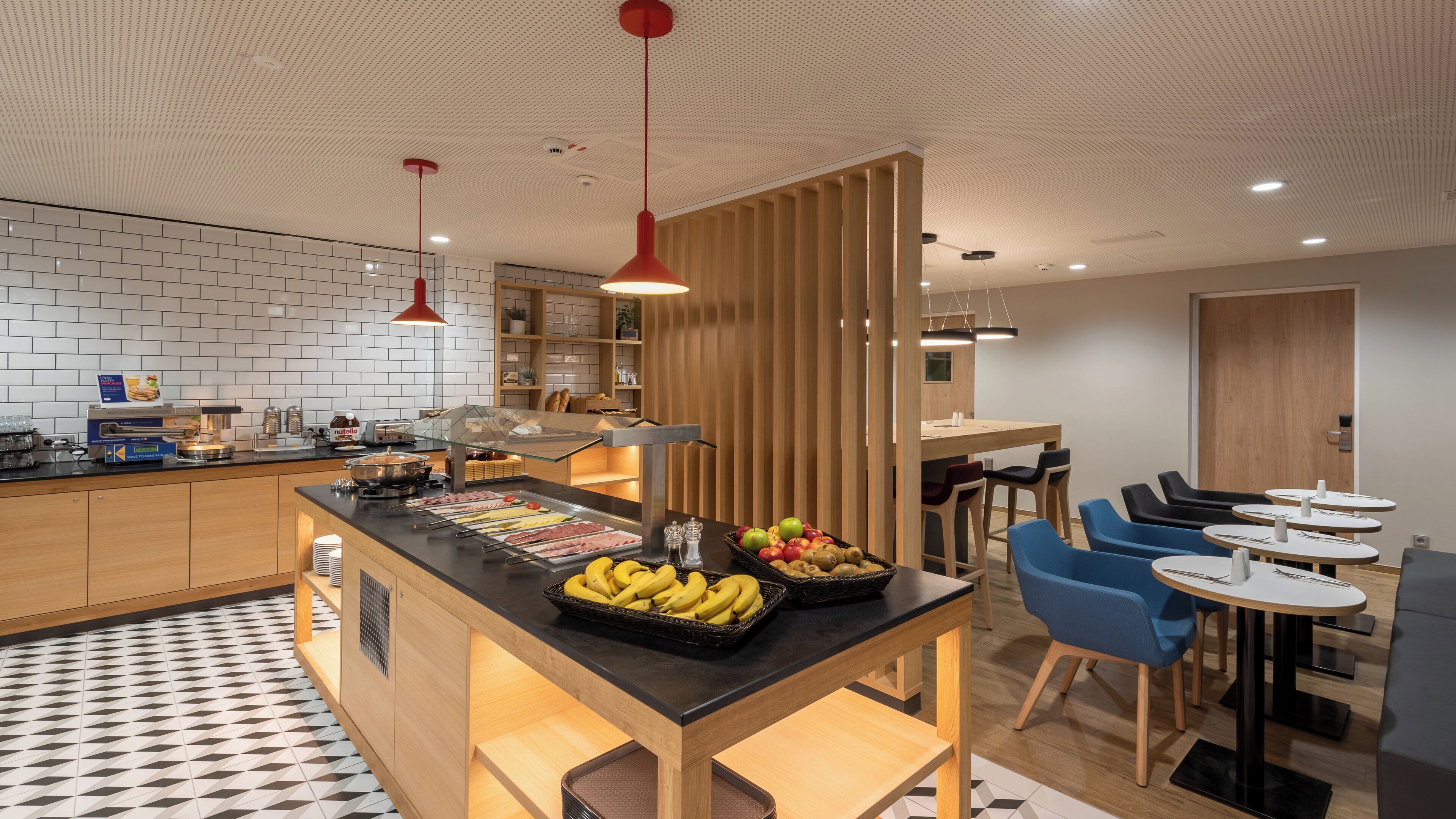 Cocina moderna con una isla central, barra desayunadora y comedor con sillas azules y mesas redondas.