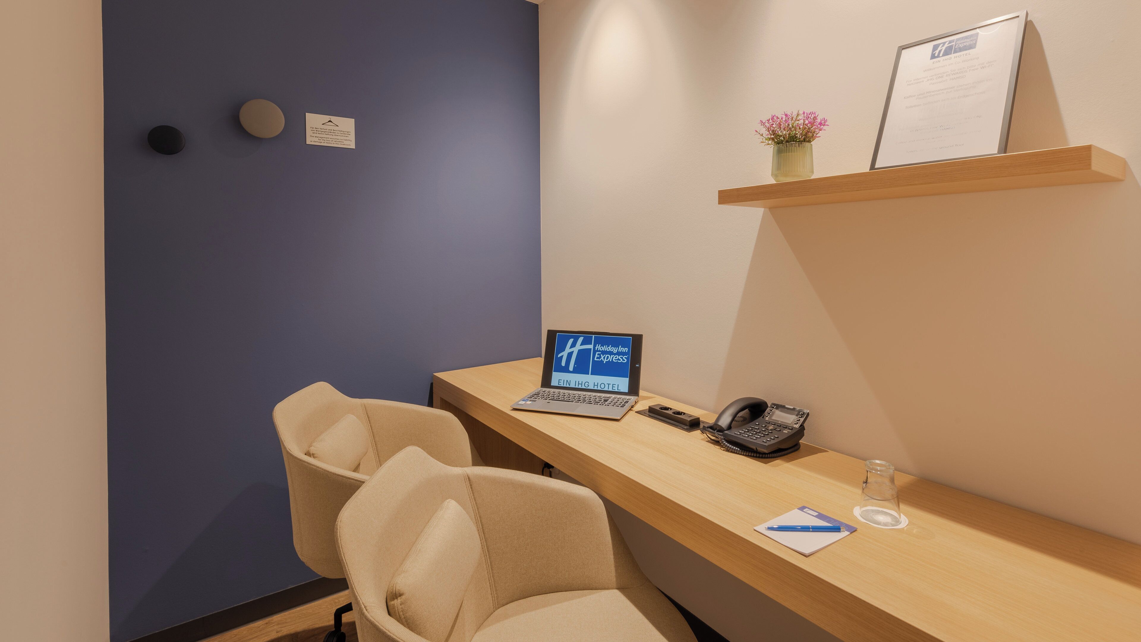 Un comptoir de réception d’hôtel avec un ordinateur portable, un téléphone et un petit vase de fleurs.