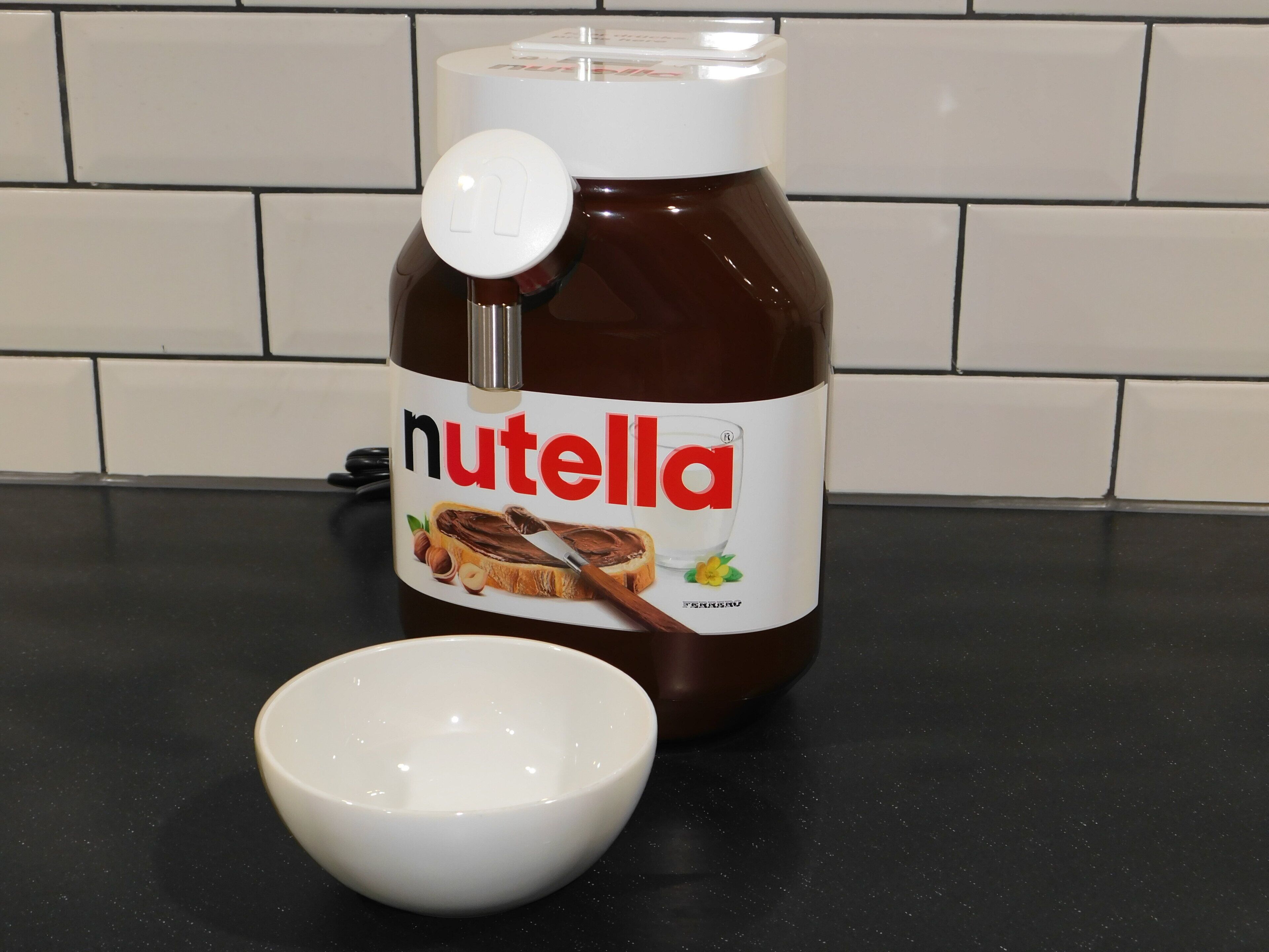Un tarro de Nutella con tapa blanca y un bol blanco sobre una encimera negra.