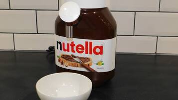 Un tarro de Nutella con tapa blanca y un bol blanco sobre una encimera negra.