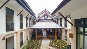 A covered walkway with a tiled roof, wooden benches, and flower beds. - Peacock De Pai Hotel (Pai)