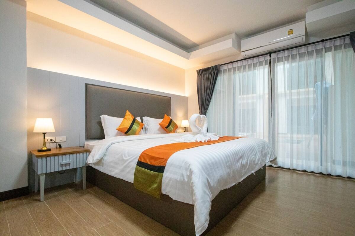 Ein Hotelzimmer mit Bett, Nachttischen, einer Lampe, Vorhängen und einer Klimaanlage.
