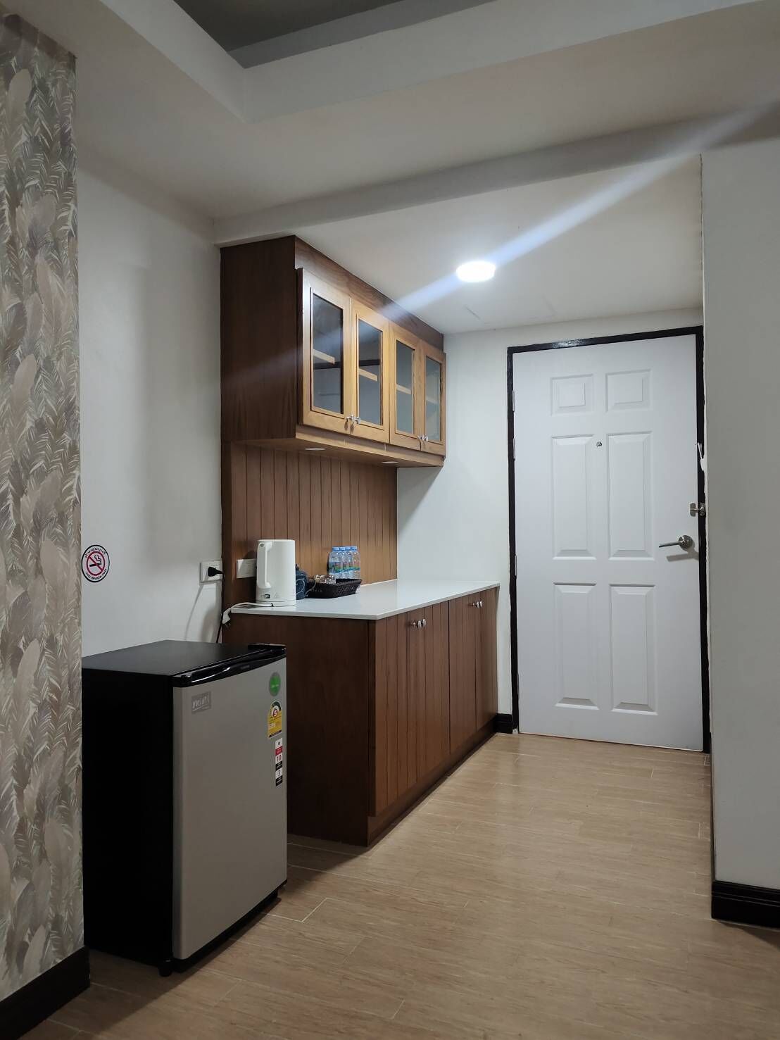 A compact kitchen with wooden cabinets, a refrigerator, and a white door.