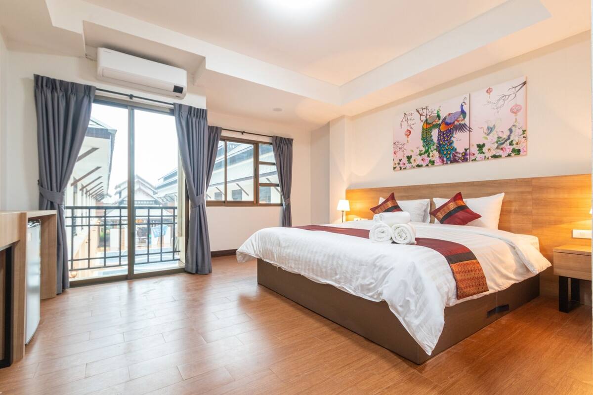 Ein Hotelzimmer mit einem großen Bett, einem Schreibtisch, einem Fenster mit Vorhängen und einem Wandbild.