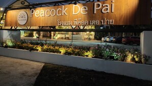 The exterior of Peacock De Pai hotel with a wooden facade and a sign in both English and Thai. - Peacock De Pai Hotel (Pai)