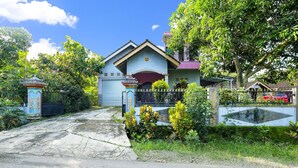 A residential house with a gated entrance, a driveway, and lush greenery.