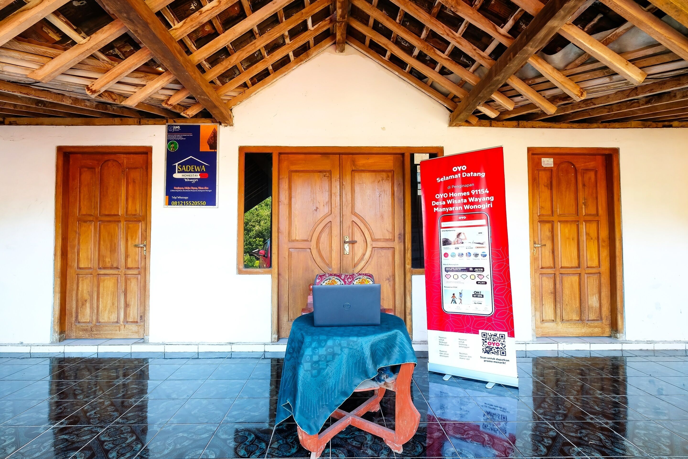 A building entrance with a wooden door, a laptop on a table, and a red informational poster.