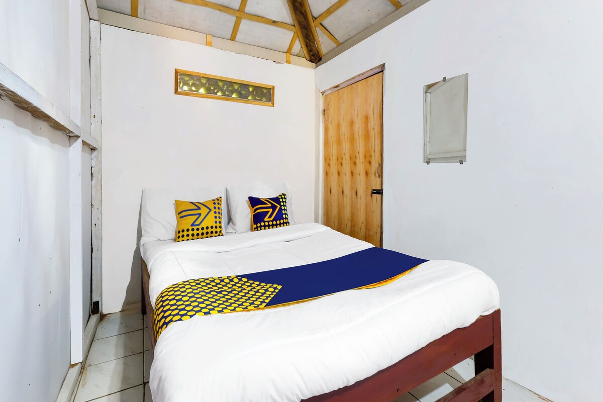 Een slaapkamer met een bed, witte muren, een houten deur en een klein raam.