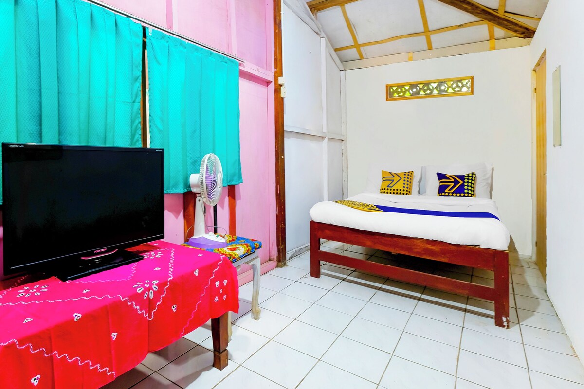 Une chambre avec un lit, une télévision, un ventilateur et une table recouverte d’une nappe rouge.