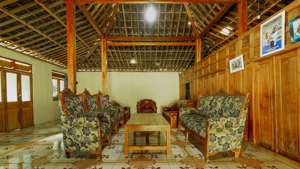 A traditional room with a wooden ceiling, patterned floor tiles, and a central wooden table surrounded by floral-patterned chairs.