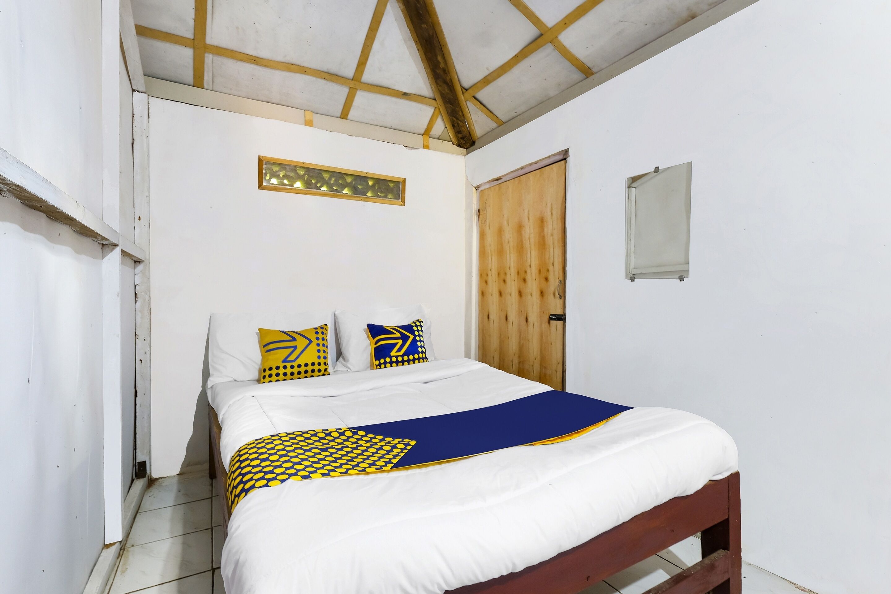 Un dormitorio con cama, puerta de madera y una ventana pequeña.