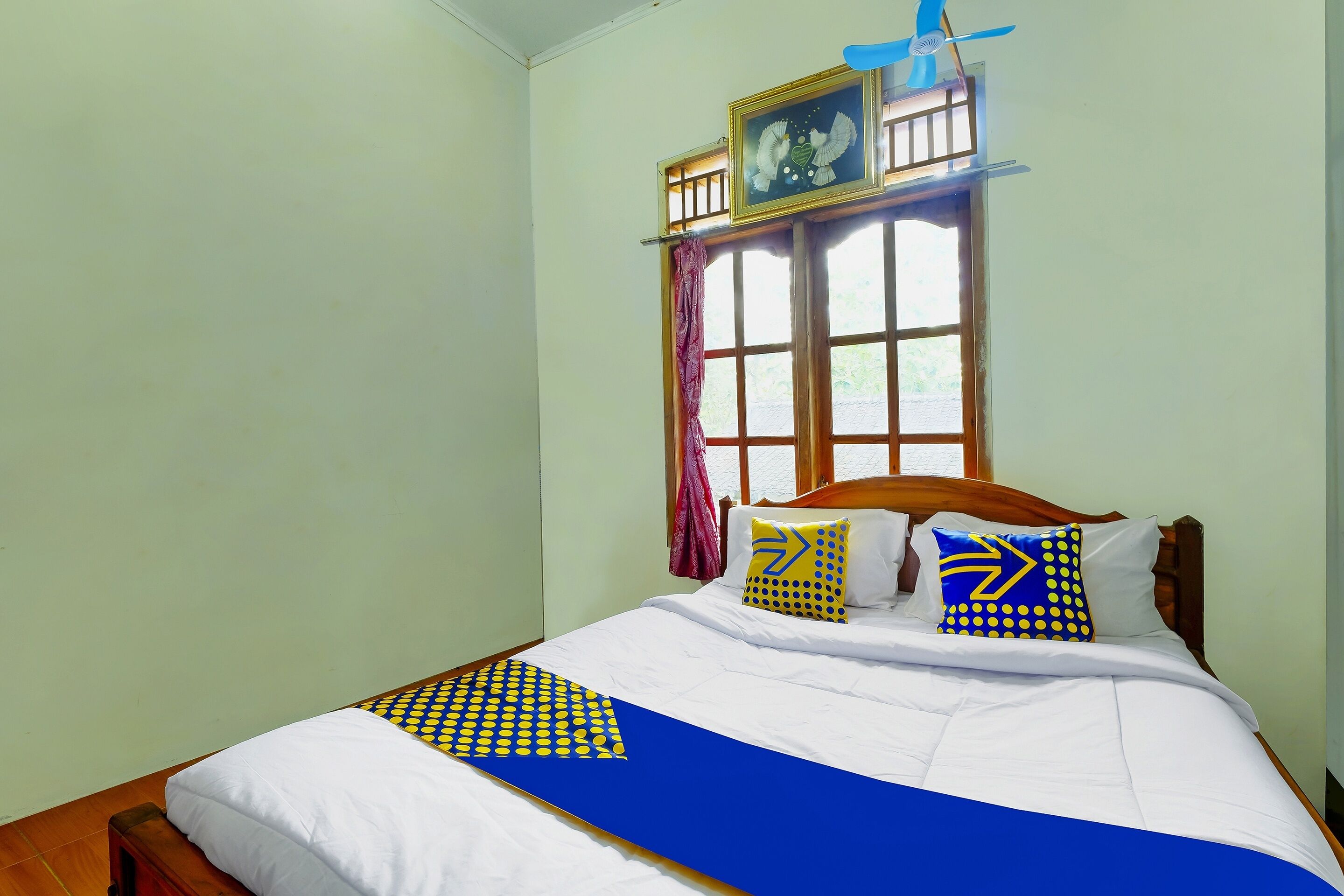 Una cama bien hecha con ropa de cama blanca y azul, un cabecero de madera y dos almohadas con diseños azules y amarillos.
