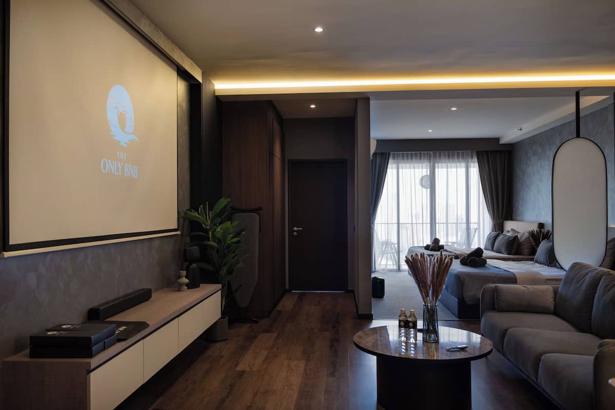 Ein modernes Wohnzimmer mit einem großen Bildschirm, der das Logo "THE ONLY BNB" zeigt, Holzboden, Sofa, Couchtisch mit Dekoration und minimalistischem Design.