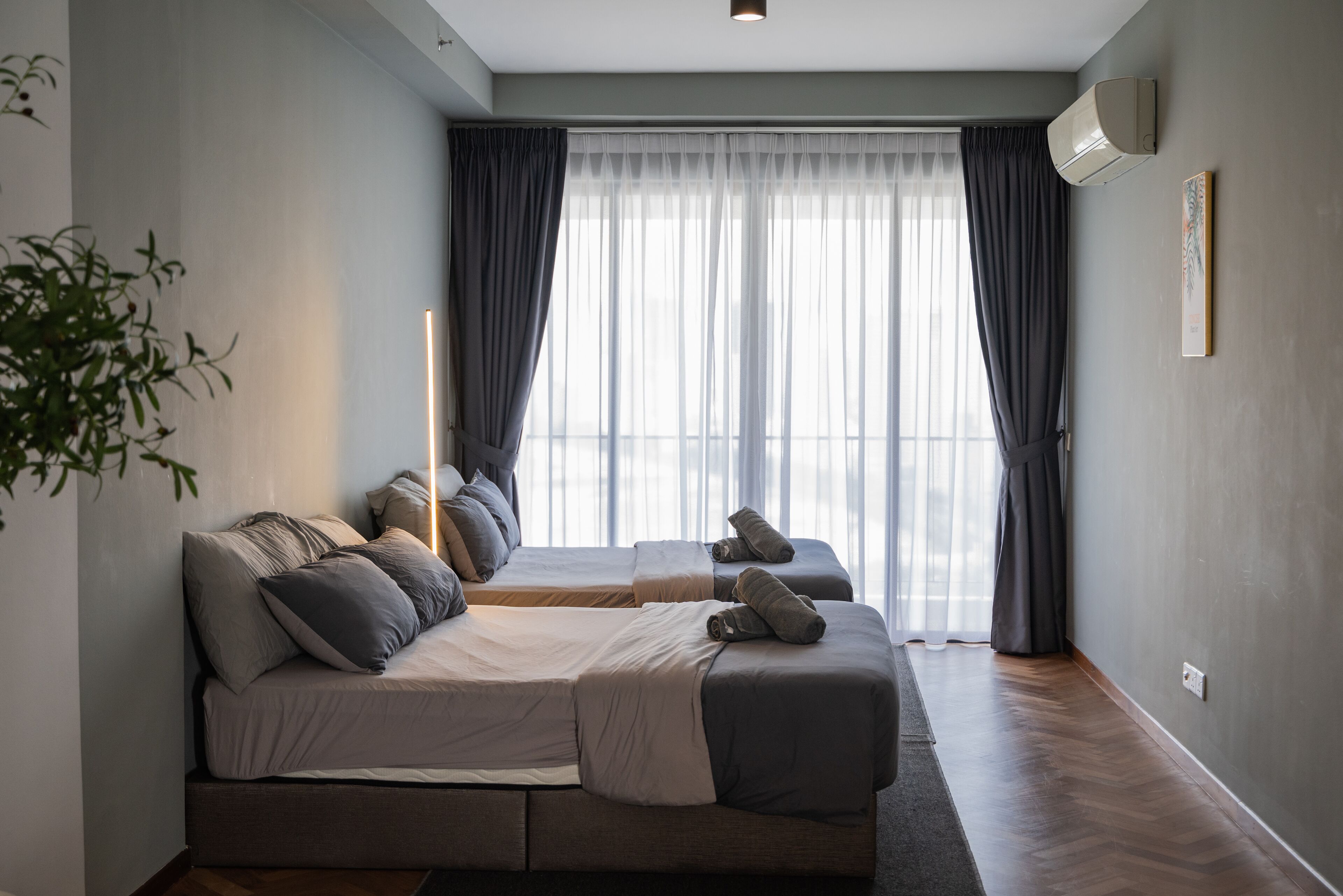 Un dormitorio moderno con una cama grande, una mesita de noche, aire acondicionado instalado en la pared y una ventana con cortinas traslúcidas.