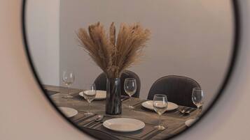A round mirror reflecting a dining table with a vase of dried plants, wine glasses, and cutlery.