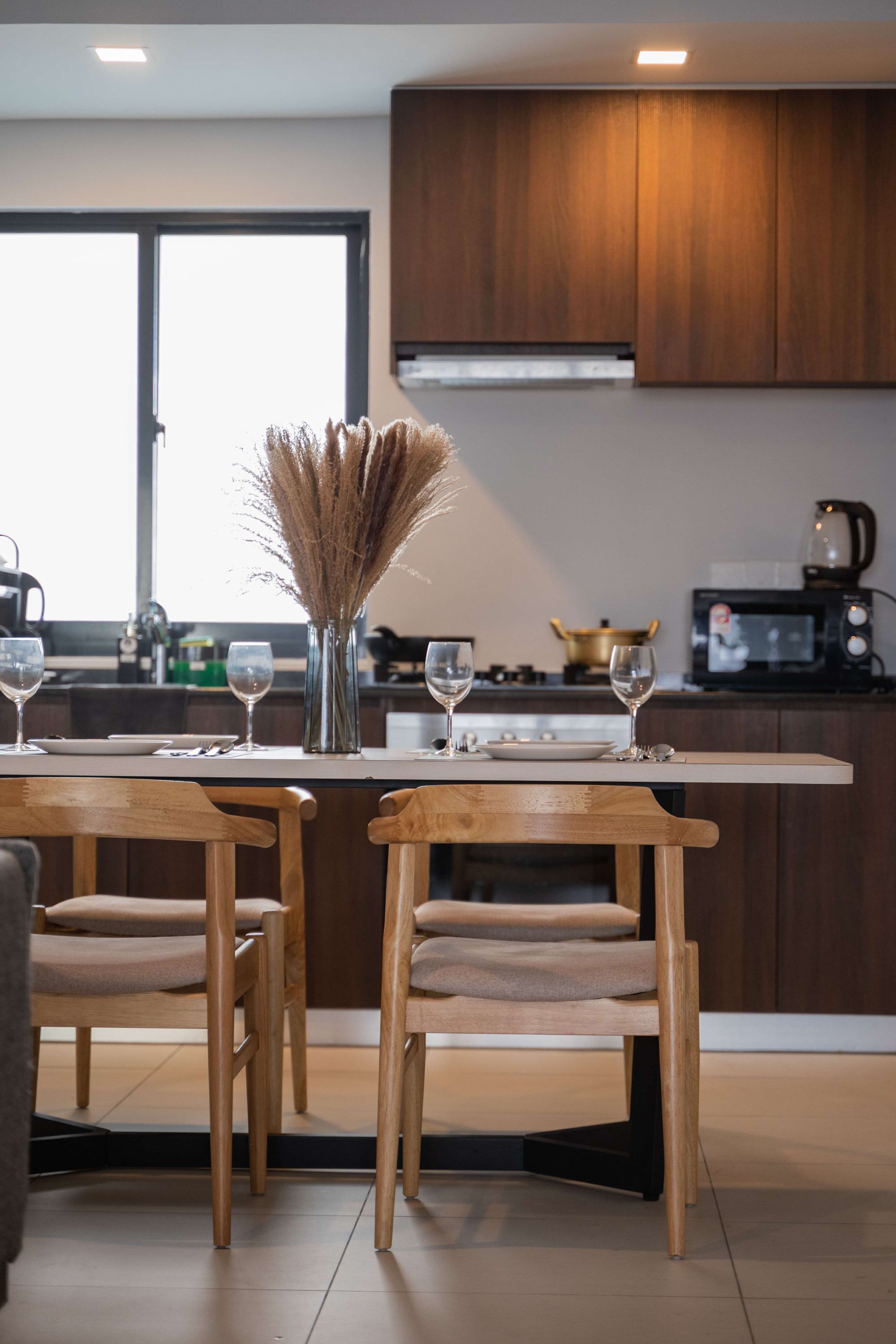 A modern kitchen with wooden cabinets, a dining table with chairs, and a vase with dried plants.