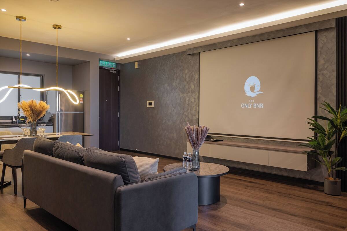 Ein moderner Empfangsbereich mit grauem Sofa, rundem Couchtisch und einer Projektionsleinwand, die ein Logo zeigt.