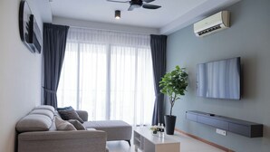 Una sala de estar moderna con un sofá gris, una mesa de centro blanca, una planta en maceta y un televisor de pantalla plana montado en la pared.