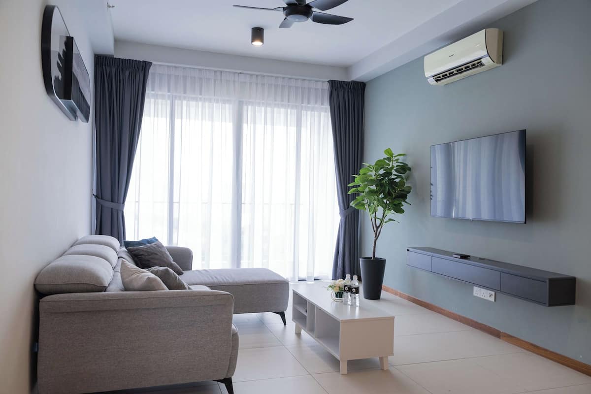 Ein modernes Wohnzimmer mit grauem Sofa, weißem Couchtisch, einer Topfpflanze und einem flachbildfernseher an der Wand.