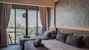 Habitación de hotel con dos camas, un ventanal amplio y vistas a la ciudad, y un cabecero moderno.