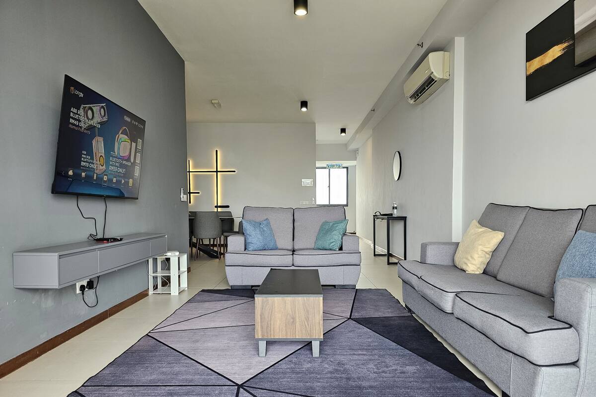 Ein modernes Wohnzimmer mit einem grauen Sofa, einem Couchtisch und einem an der Wand befestigten Fernseher.