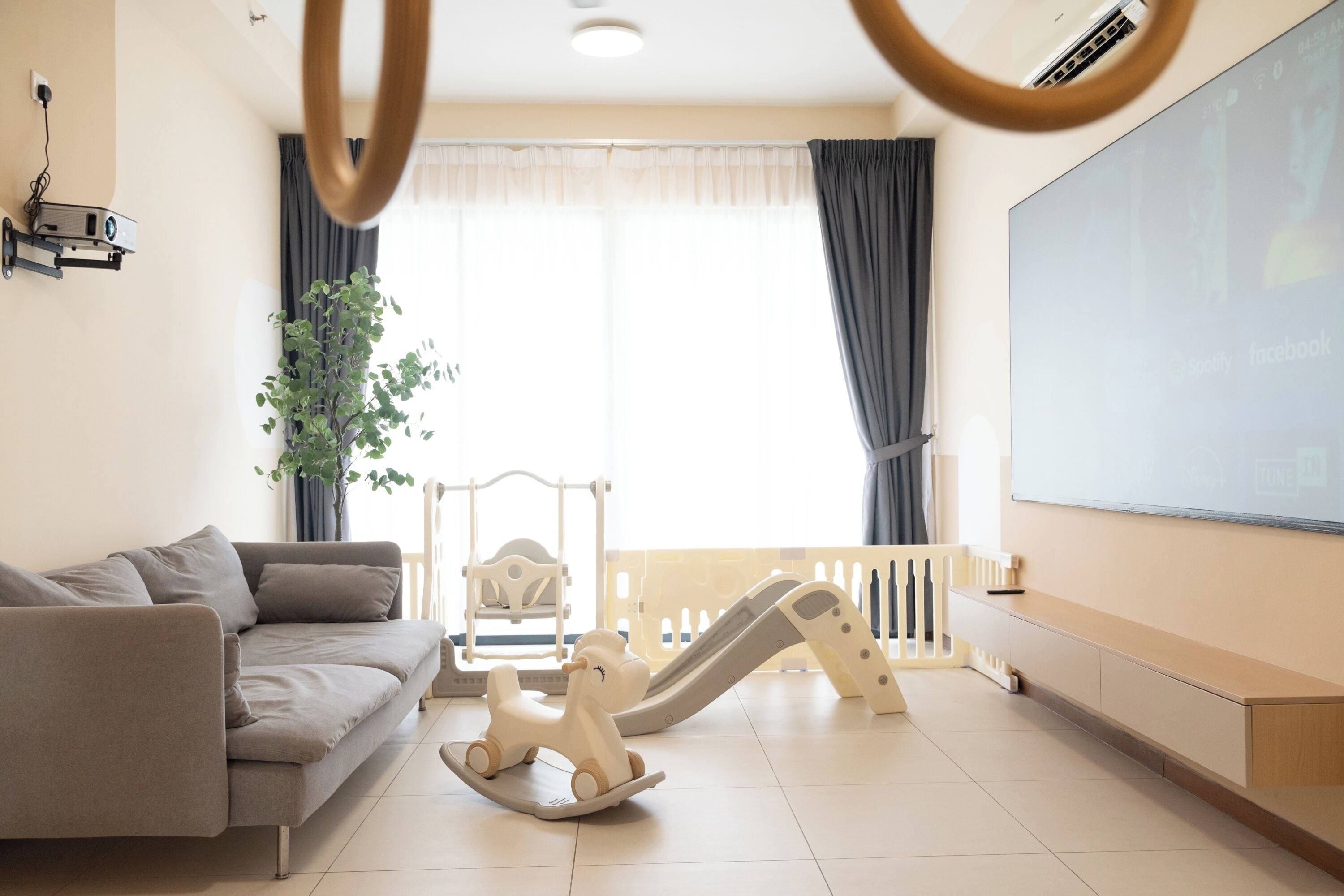A living room with a sofa, a playpen, a projector, and a large screen.