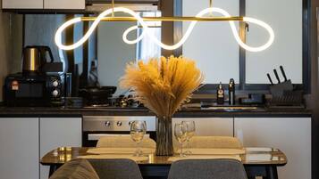 A modern kitchen with a dining area, featuring a sofa, a table with wine glasses, and a vase with dried flowers.