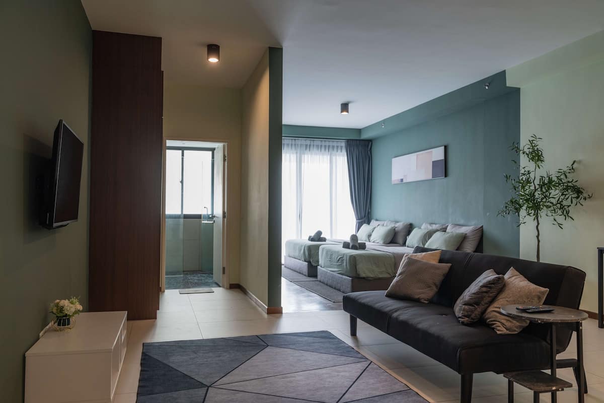 Ein modernes Wohnzimmer mit einer Couch, einem Couchtisch und einem Fernseher. Ein Bett bietet Blick ins Freie.