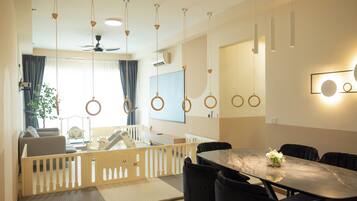 Una sala de estar moderna con comedor, que cuenta con techo alto, lámparas colgantes, ventilador de techo y un gran ventanal con cortinas.