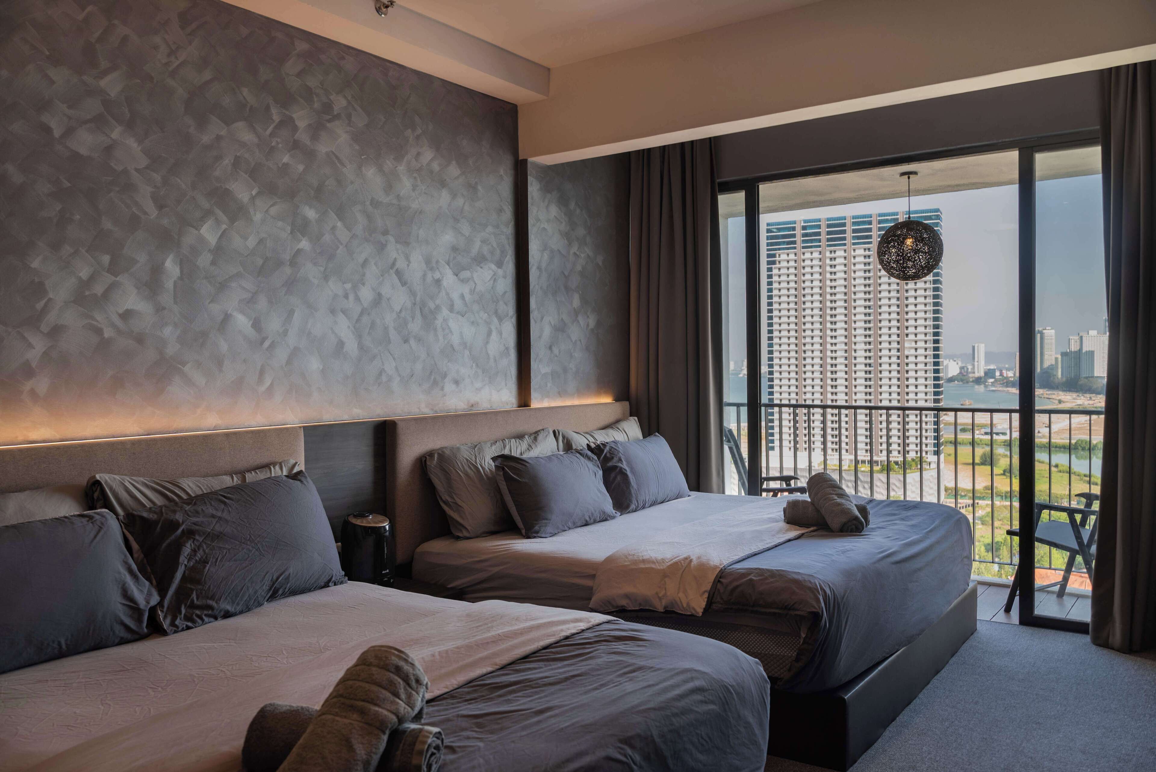 Una habitación de hotel moderna con dos camas, un ventanal y vistas a la ciudad, y un balcón con vistas al horizonte urbano.