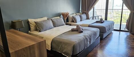 A modern bedroom with two beds, a wooden desk, and a view of a cityscape through large windows.