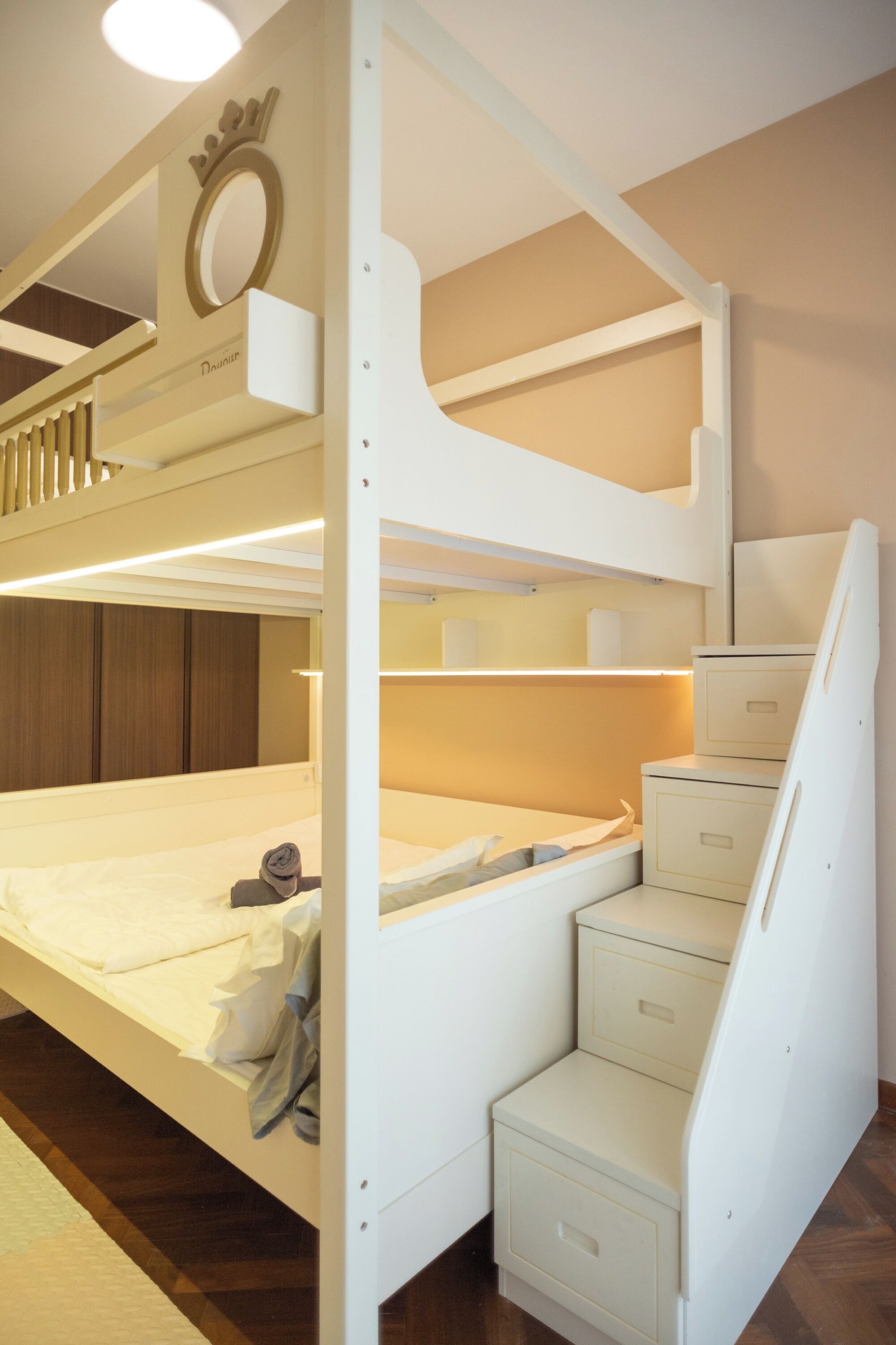 Una cama litera con cabecera que incluye un símbolo de corona y la palabra "Dourado". Hay cajones debajo de la cama y una pequeña zona de escritorio.