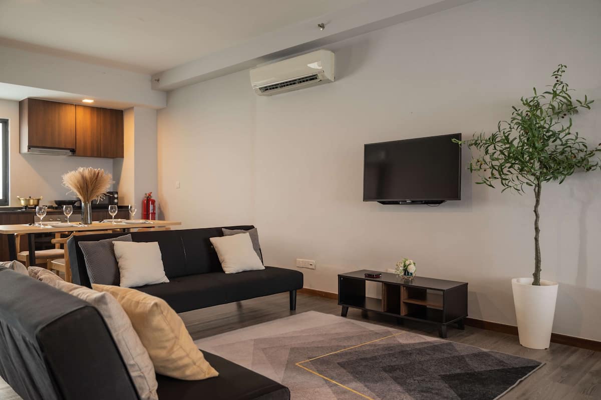 Ein modernes Wohnzimmer mit einem schwarzen Sofa, einem Couchtisch und einer großen Küstertopf-Pflanze.