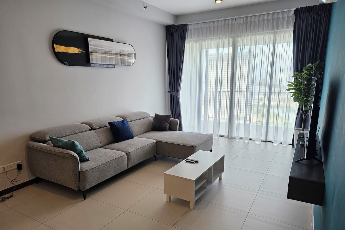 Ein modernes Wohnzimmer mit einem grauen Ecksofa, einem weißen Couchtisch und einem großen Fenster mit transparenten Vorhängen.
