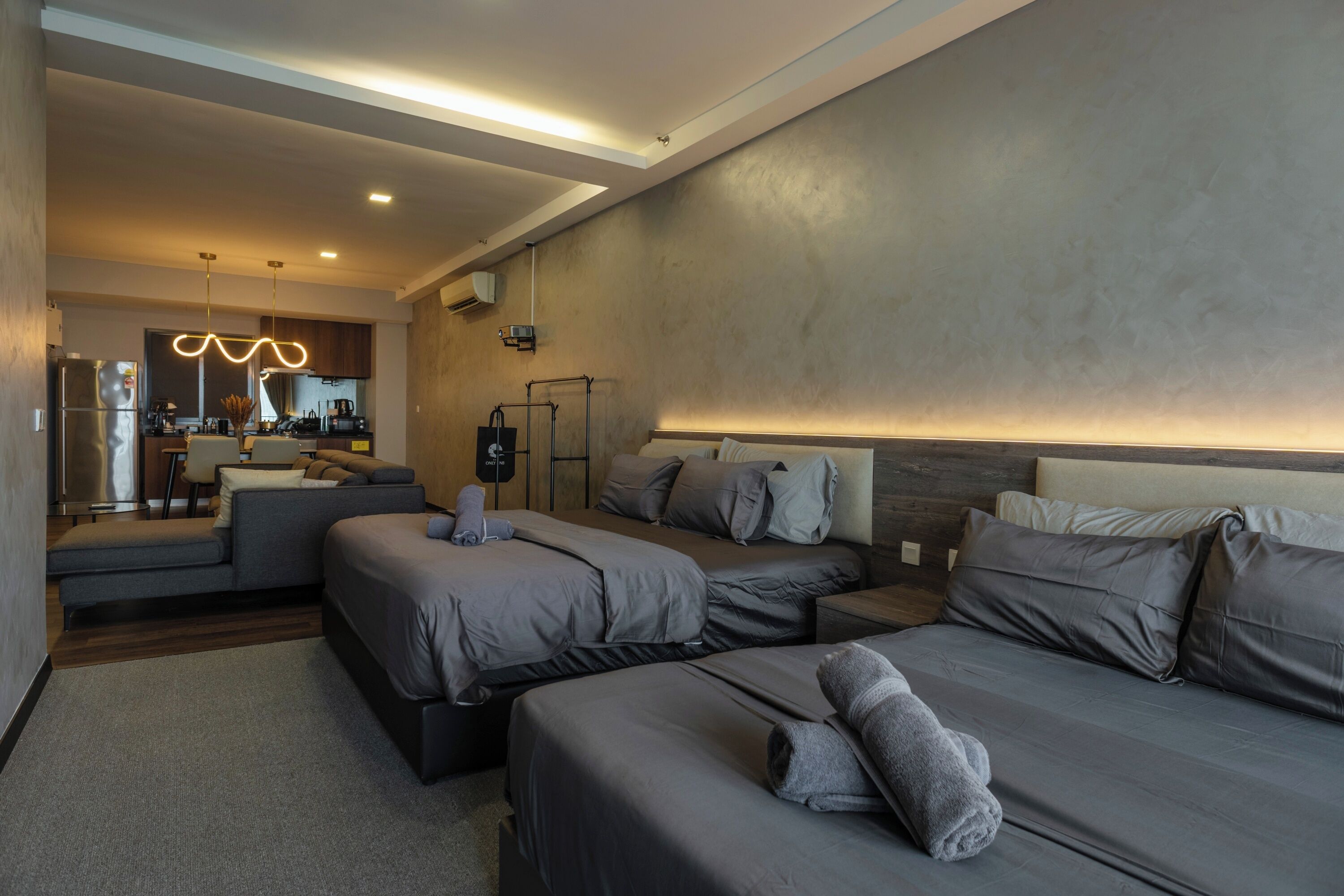 A modern hotel room with a sofa, two beds, a small kitchenette, and a large mirror.