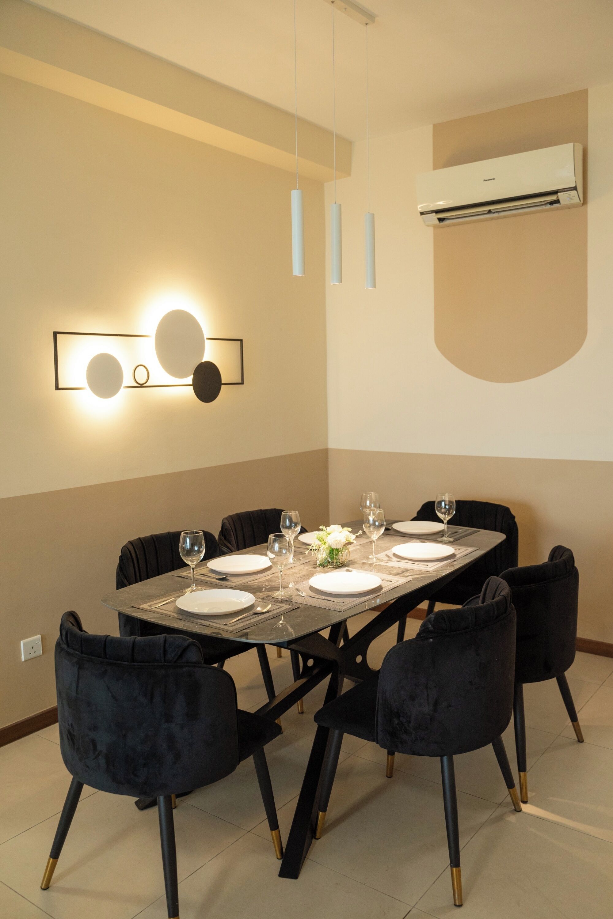 A dining area with a rectangular table set for six, surrounded by six black chairs with gold accents.