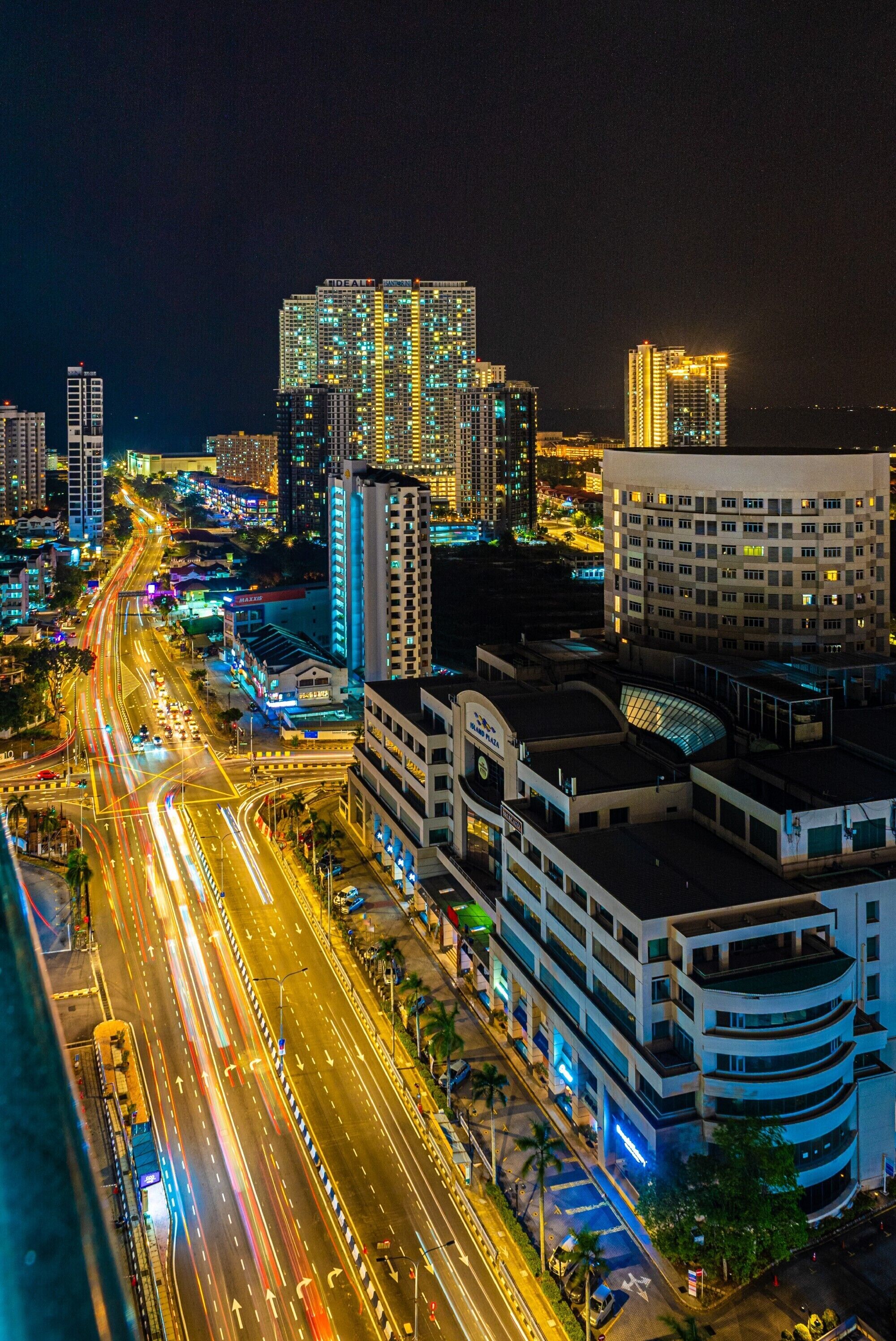A nighttime cityscape with illuminated high-rise buildings and a busy multi-lane road.
