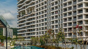 Un hotel moderno con zona de piscina, que presenta un edificio grande de varios pisos con balcones y una piscina azul cristalina.