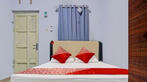 Ein Bett mit einer weißen Matratze und rot-weißer Bettwäsche, einem beigen Kopfteil und zwei roten Kissen.