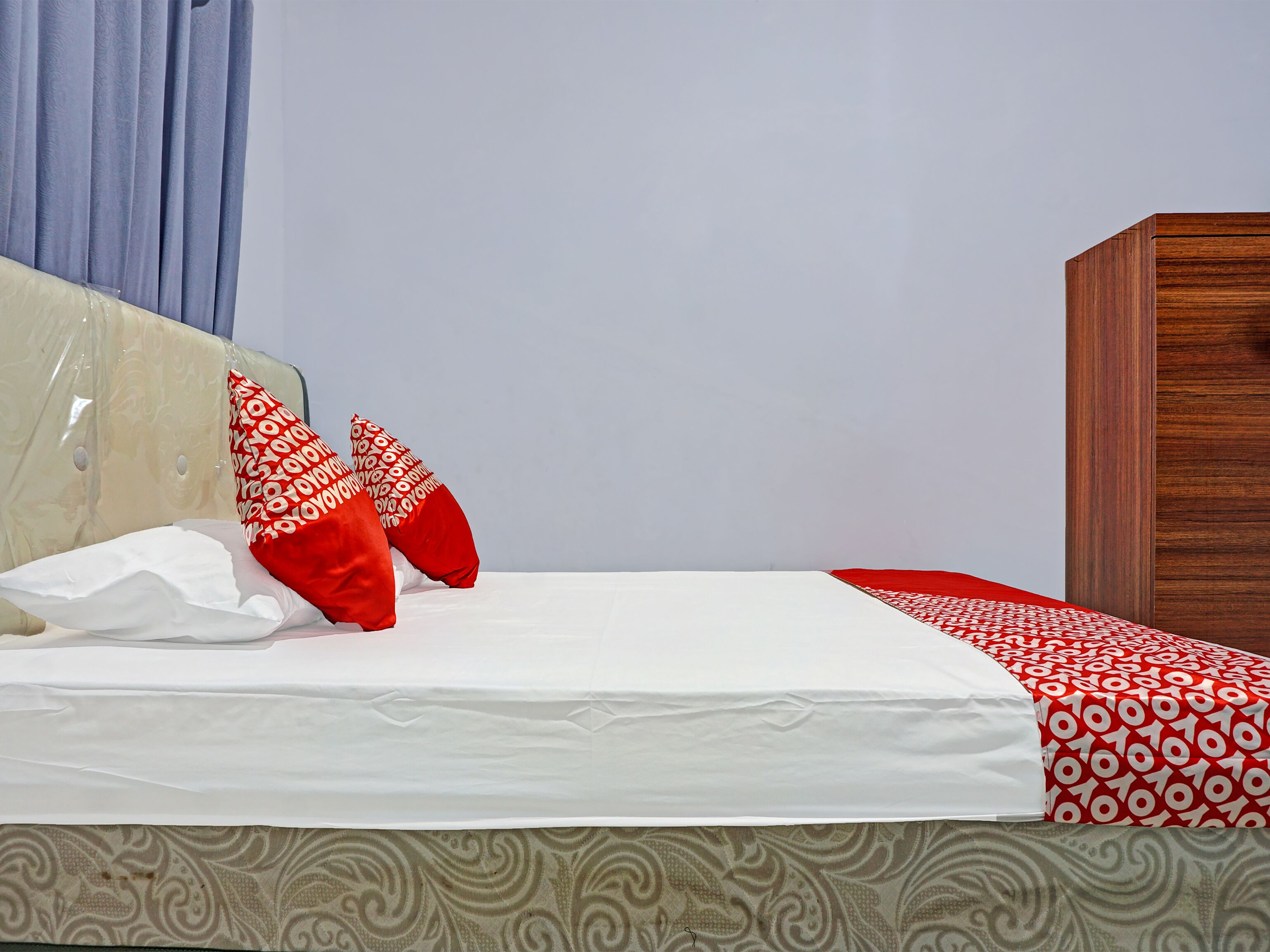 Un lit bien fait, avec une literie blanche et rouge, une tête de lit en bois et un mur décoré d’un motif.