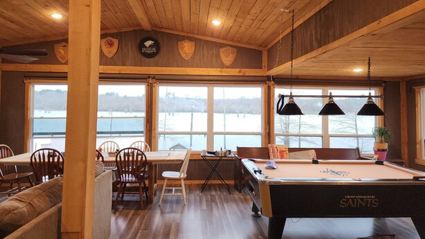 Un intérieur en bois avec une table de billard, des chaises et de grandes fenêtres donnant sur un lac.