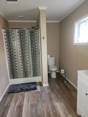 A bathroom with a shower, toilet, and a window.