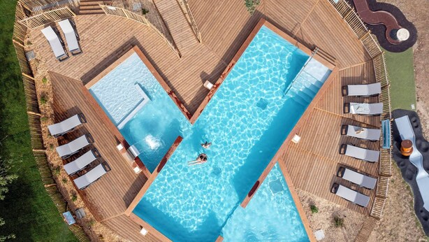 An aerial view of a pool area with two separate swimming pools, deck chairs, and lounge areas.