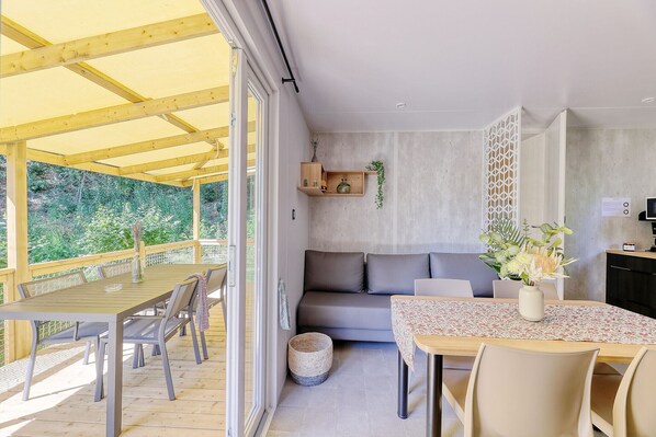 Un interior moderno con una mesa de comedor de madera, sofá gris y una pequeña zona de cocina.