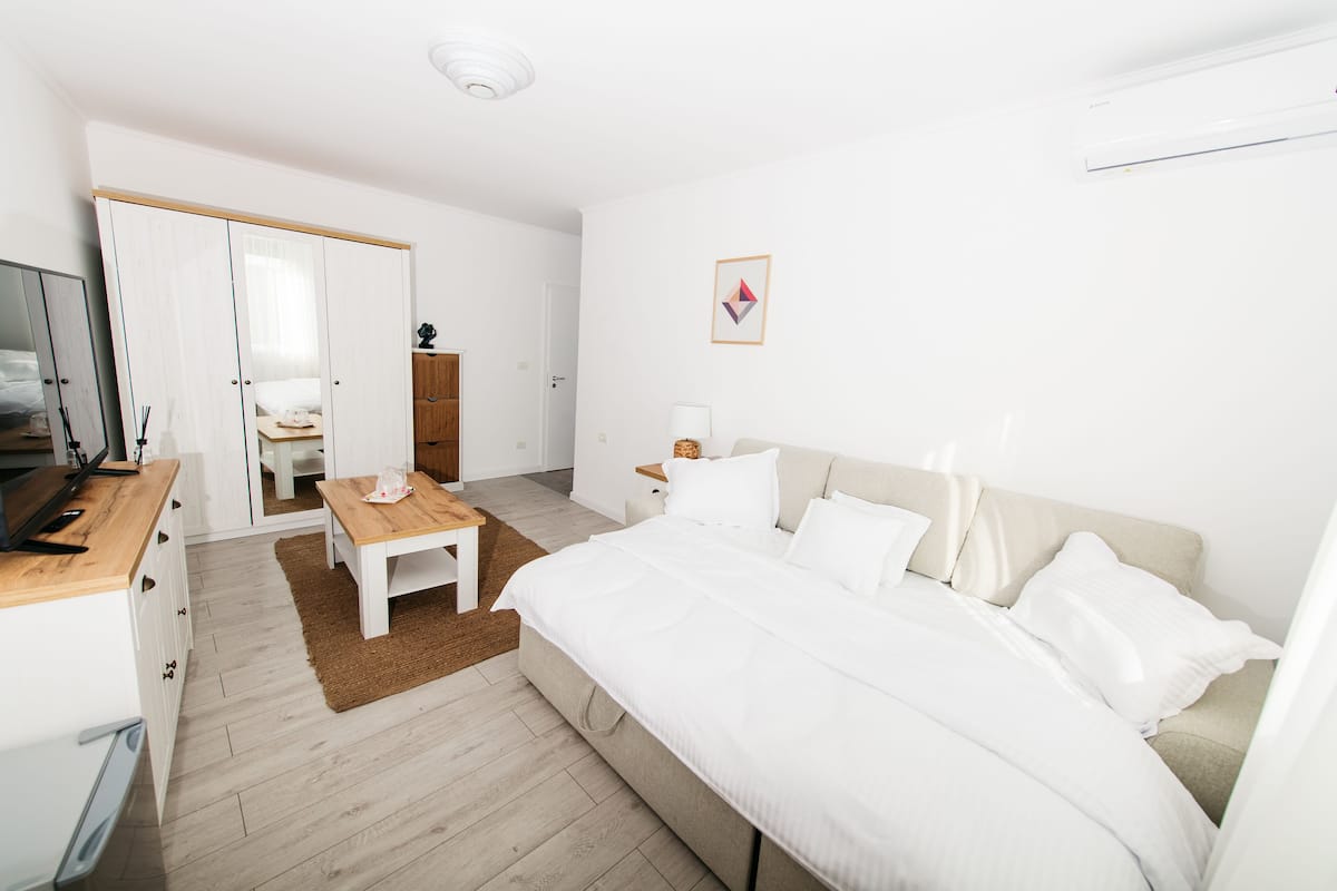 A modern bedroom with a large bed, a wooden nightstand, a desk, and a wardrobe.