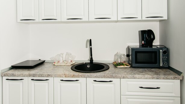 A kitchen with white cabinets, a microwave, a coffee maker, and a scale on the counter. - EVRA APARTMENTS (Recas)